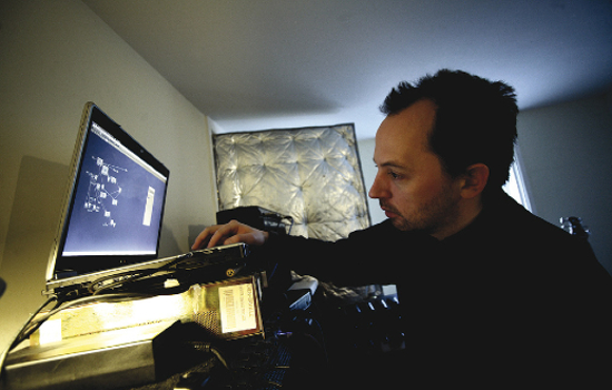 A man with short black hair and short facial hair, in a bedroom using a laptop